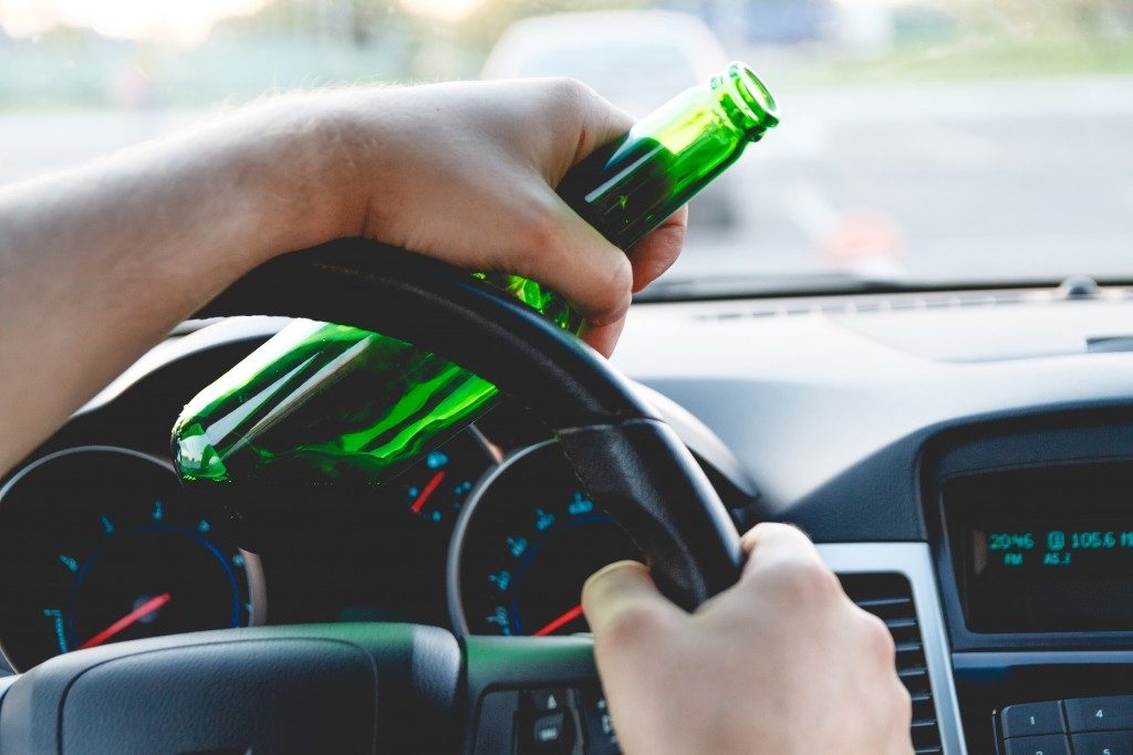 person driving with bottle in hand